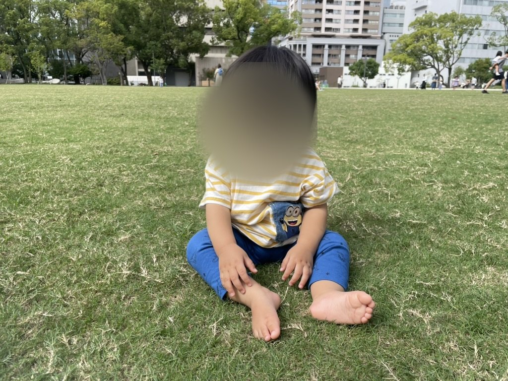 広い芝生に座って周囲を眺める1歳児